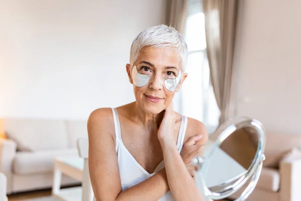 Portrait of pretty, nice grandmother with eye patches, having bags under eyes in the morning because of less sleep, showing an effect of perfect skin