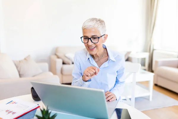 Woman wearing glasses at home concentrating as she works on a laptop. Middle-aged woman working from home on laptop. Portrait of executive mature woman typing on laptop while working at home.