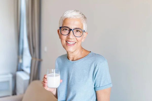 Portrait of a senior woman with a glass of milk. Beautiful elderly woman in grey T-shirt with a glass of milk. Senior woman drinking milk at home