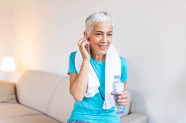 Senior woman with headphones while resting after workout. Athletic mature woman resting after a good workout session