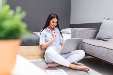 Young businesswoman sitting on the floor with laptop and working. Beautiful woman working at home, using laptop, smiling and looking at laptop