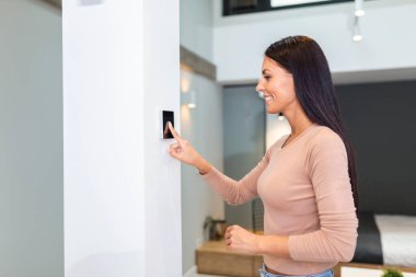 Woman using smart wall home control system in modern apartment. woman touching the display and controlling smart home system hanging on the wall in her apartment