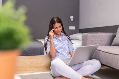 Young businesswoman sitting on the floor with laptop and working. Beautiful woman working at home, using laptop, smiling and looking at laptop