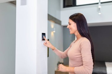 Woman using smart wall home control system in modern apartment. woman touching the display and controlling smart home system hanging on the wall in her apartment
