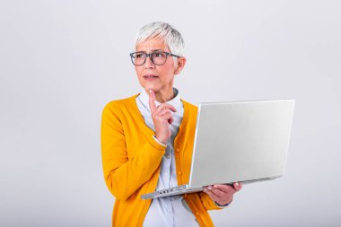 Photo of a thinking mature business woman isolated over grey background holding laptop computer. Image of confused senior woman using laptop computer. Looking at laptop while holding face with hands.