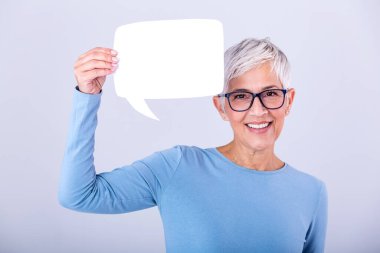 Happy mature woman in plain blue long sleeve t-shirt holding empty speech bubble isolated on background. Woman showing sign speech bubble banner looking happy