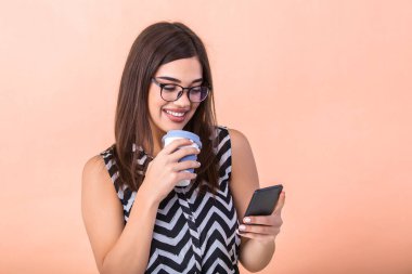 Young smart successful woman in glasses having break, holding coffe to go and surfing the internet with her mobile smart phone