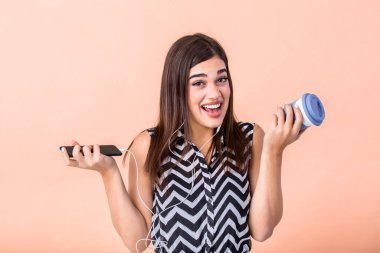 Woman with a paper cup of coffee in one hand and smart phone in other. Brunette girl with dark hair drinking coffee and surfing the net. Happy woman expression