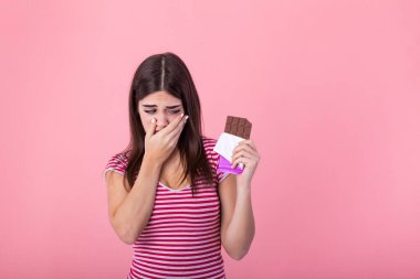 Portrait sad young woman tired of diet restrictions craving sweets chocolate isolated on pink wall background. Human face expression emotion. Nutrition concept. Feeling of guilt. Passion for chocolate