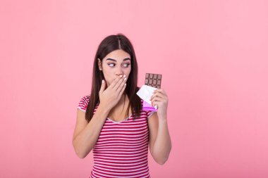 Portrait of a happy young woman with chocolate bar isolated over pink background covenring her mouth. Young woman with natural make up having fun and eating chocolate isolated on pink background