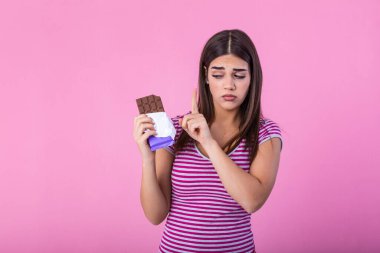 Portrait of a serious pretty girl refusing to eat chocolate bar with a hand gesture , serious pretty girl refusing to eat chocolate bar with a hand gesture isolated over pink background