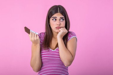 Portrait sad young woman tired of diet restrictions craving sweets chocolate isolated on pink wall background. Human face expression emotion. Nutrition concept. Feeling of guilt. Passion for chocolate