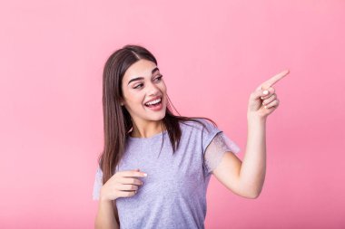 Portrait of brunette woman with long hair in basic t-shirt rejoicing and pointing finger at copyspace isolated over pink background