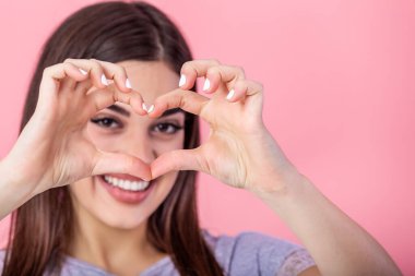Close-up portrait of cheerful attractive woman showing heart gesture, looking at camera, isolated on pink background
