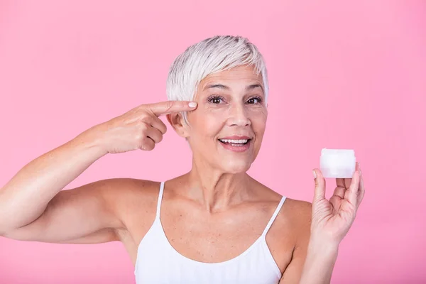 Smiling senior woman applying anti-aging lotion to remove dark circles under eyes. Mature woman using cosmetic cream to hide wrinkles. Lady using day moisturizer to counteract the aging of the skin.