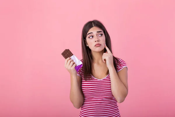 Teenage girl with acne problem holding chocolate bar against pink background. Young beautiful Woman Acne Problem Face with Chocolate bar UnHappy Eating,His Stressful face.