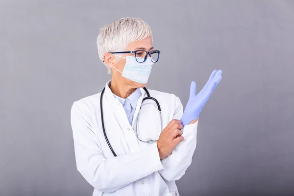 Senior female Doctor putting on protective gloves and mask, isolated on background. Doctor putting on sterile gloves