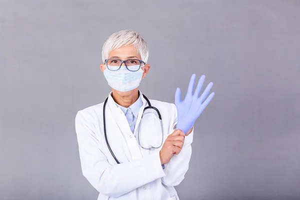 Senior female Doctor putting on protective gloves and mask, isolated on background. Doctor putting on sterile gloves