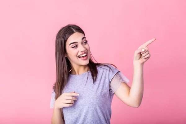 stock image Portrait of brunette woman with long hair in basic t-shirt rejoicing and pointing finger at copyspace isolated over pink background