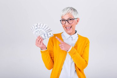 Happy senior woman holding lots of cash, elderly woman with one hundred dollar bills on white background and pointing with her finger on money clipart