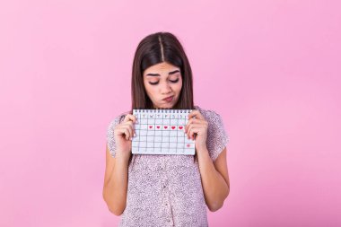 Portrait of disappointed outraged woman 20s holding period calendar isolated over pink background in studio. Beautiful young woman standing isolated over pink background, showing menstrual calendar