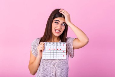 Young beautiful woman holding menstruation calendar over isolated background with surprise face. Young girl holding menstruation calendar with confused face, afraid and excited with fear expression