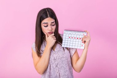 Young beautiful woman holding menstruation calendar over isolated background with surprise face. Young girl holding menstruation calendar with confused face, afraid and excited with fear expression