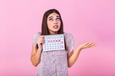 Portrait of young woman in dress, holding female periods calendar for checking menstruation days isolated on trending pink background. Medical healthcare, gynecological concept.