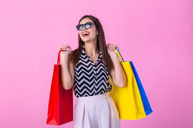 Portrait of an excited beautiful girl wearing fashionable and sunglasses holding shopping bags isolated over pink background