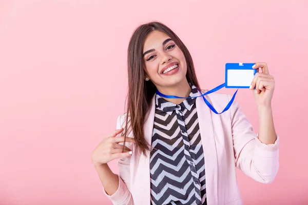 Beautiful success woman shows on camera her badge and smiling over pink wall. Young attractive woman holding blank artist lanyard or badge in hand with metal piece. Plastic pass concept.