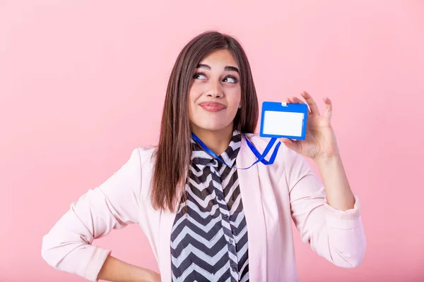 Beautiful success woman shows on camera her badge and smiling over pink wall. Young attractive woman holding blank artist lanyard or badge in hand with metal piece. Plastic pass concept.