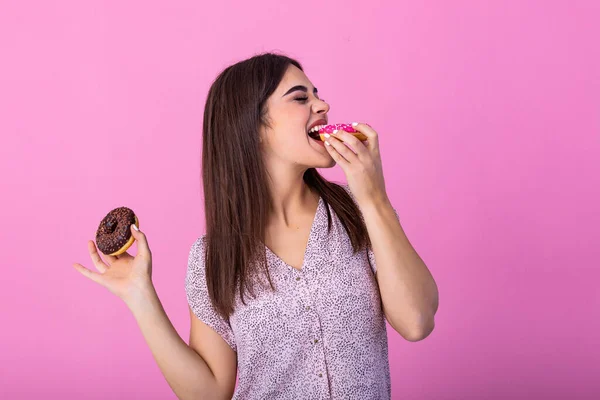 Beauty model girl eating colorful donuts. Funny joyful Vogue styled woman choosing sweets on pink background. Diet, dieting concept. Junk food, Slimming, weight loss