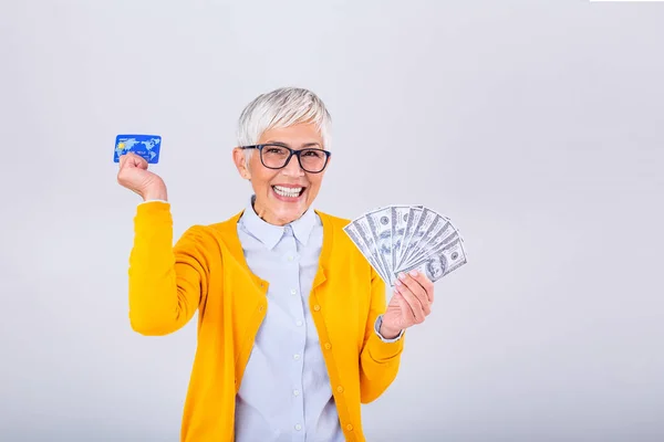 Closeup portrait super happy excited successful senior woman pensioner holding money dollar bills and credit card in hand. Positive emotion facial expression feeling. online shopping