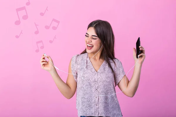 Happy young woman wearing headphones listening to music from smartphone studio shot isolated on pink background with music notes. excited young woman having fun in headphones with phone on pink studio background.