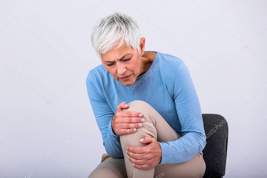 Senior woman holding the knee with pain. Old age, health problem and people concept - senior woman suffering from pain in leg at home. Elderly woman suffering from pain in knee at home