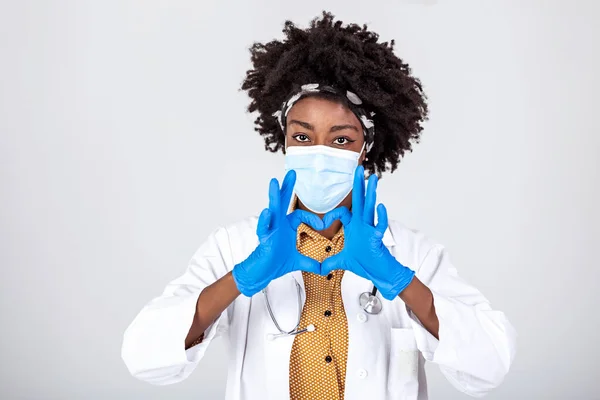 Female african professional medic nurse, doctor wear face mask, gloves, uniform showing heart hands shape. Medical love, care and safety symbol, corona virus health protection sign concept. Closeup