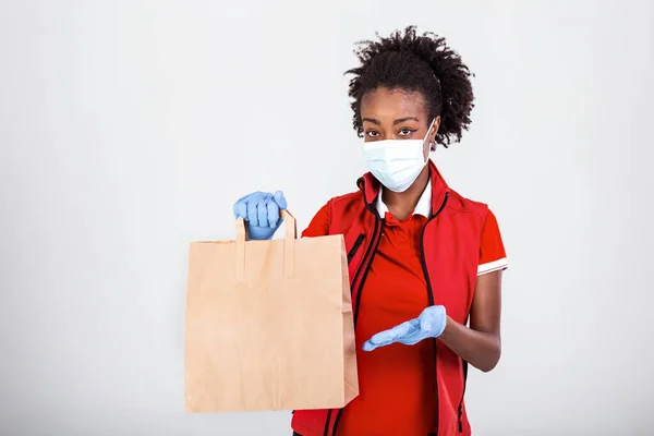 Delivery woman employee in red t-shirt uniform mask glove hold craft paper bag with food isolated on white background studio Service quarantine pandemic coronavirus virus 2019-ncov concept