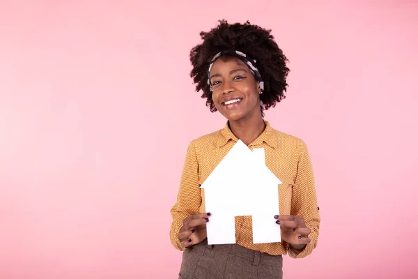 Insurance, loan, real estate and family concept. Smiling black woman buying home, holding paper house in hands and smiling, paying debt, standing pink background happy