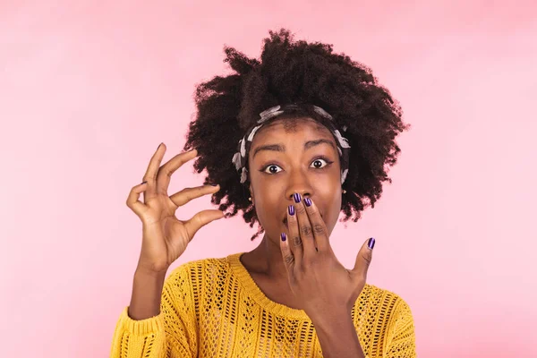 Size matters. Pleased African American young woman demonstrates very tiny object, smiles positively, wears casual sweater, poses against pink background, shapes small thing. Body language concept