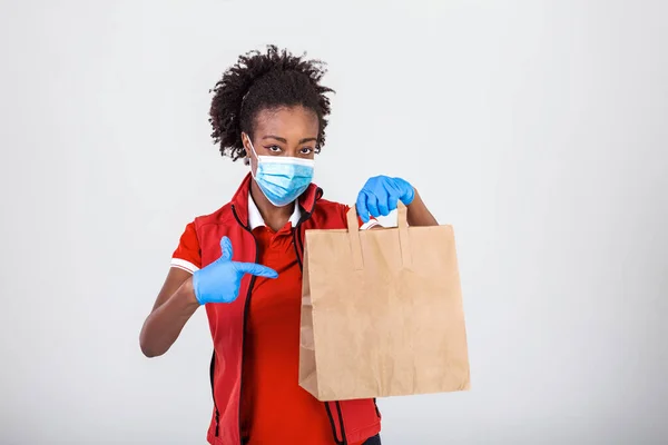 Delivery woman employee in red t-shirt uniform mask glove hold craft paper packet with food isolated on white background studio Service quarantine pandemic coronavirus virus 2019-ncov concept