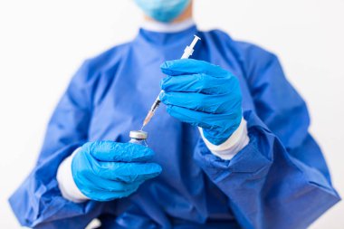 PPE süit üniformalı kadın doktor ya da bilim adamının eli laboratuarda koruyucu yüz maskesi takıyor ilaç şişesi ve şırınga, koronavirüs ya da COVID 19 kavramı izole edildi.