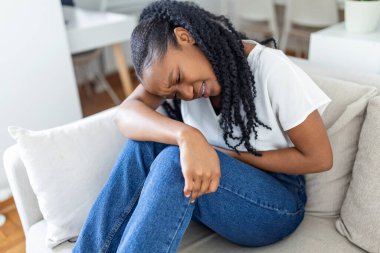 Adet gören karın ağrısına karşı el ele tutuşan, evde üzgün yatan, kadın sağlığı konseptinde mide krampı yaşayan bir kadın.