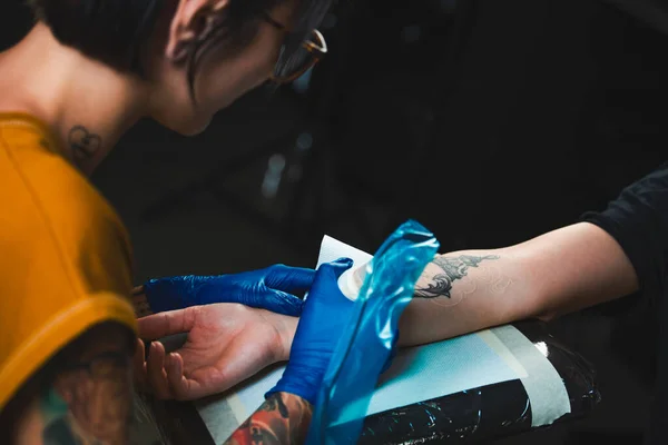 タトゥーアーティストは女の子の腕の上にタトゥーを作成します タトゥーマシンに焦点を当てます タトゥーマシンを閉めろ サロンで手に絵を描くことで — ストック写真