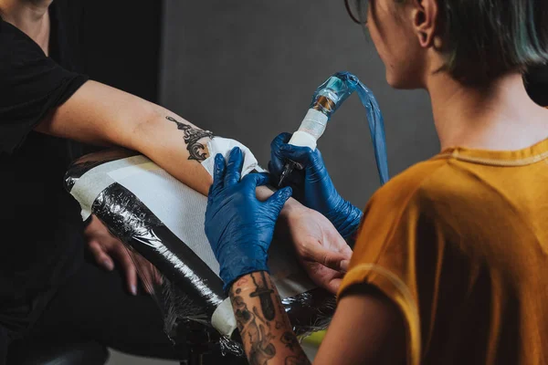 閉じタトゥーアーティストは 塗料で黒の入れ墨を取得するプロセスを示しています マスターは青滅菌手袋で動作します 入れ墨のマスターは 回路の入れ墨を埋める — ストック写真