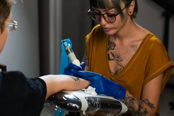 Portrait of a woman tattoo master showing a process of creation tattoo on a hand