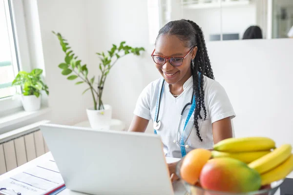 Smiling nutritionist in her office, she is showing healthy vegetables and fruits, healthcare and diet concept. Female nutritionist with fruits working at her desk.