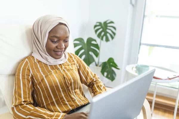 무슬림 소파에 노트북을 행복하게 있습니다 아름다운 이슬람 여성은 소파에 노트북을 — 스톡 사진