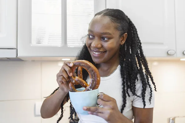 Joven Mujer Afroamericana Sentada Escritorio Cocina Disfrutando Pretzel Con Taza — Foto de Stock