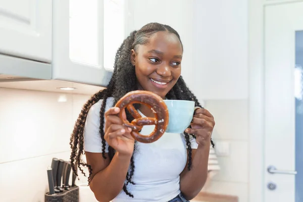 Joven Mujer Afroamericana Sentada Escritorio Cocina Disfrutando Pretzel Con Taza — Foto de Stock