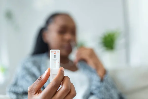 African-American woman using cotton swab while doing coronavirus PCR test at home. Woman using coronavirus rapid diagnostic test. Young woman at home using a nasal swab for COVID-19.